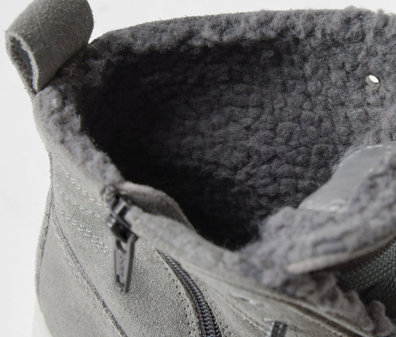 Detail šedé kotníkové boty s vnitřní kožešinou a zipem.