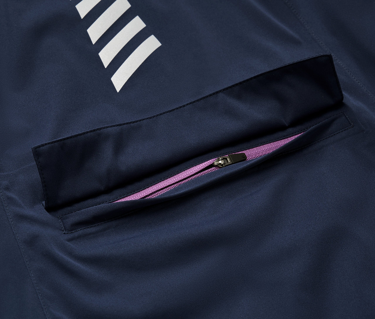 Detail tmavě modré cyklistické bundy do deště s bílými pruhy a fialovým zipem.