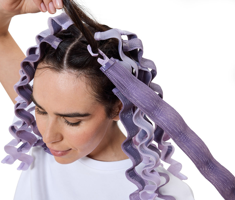 Žena si natáčí vlasy pomocí fialových natáček.