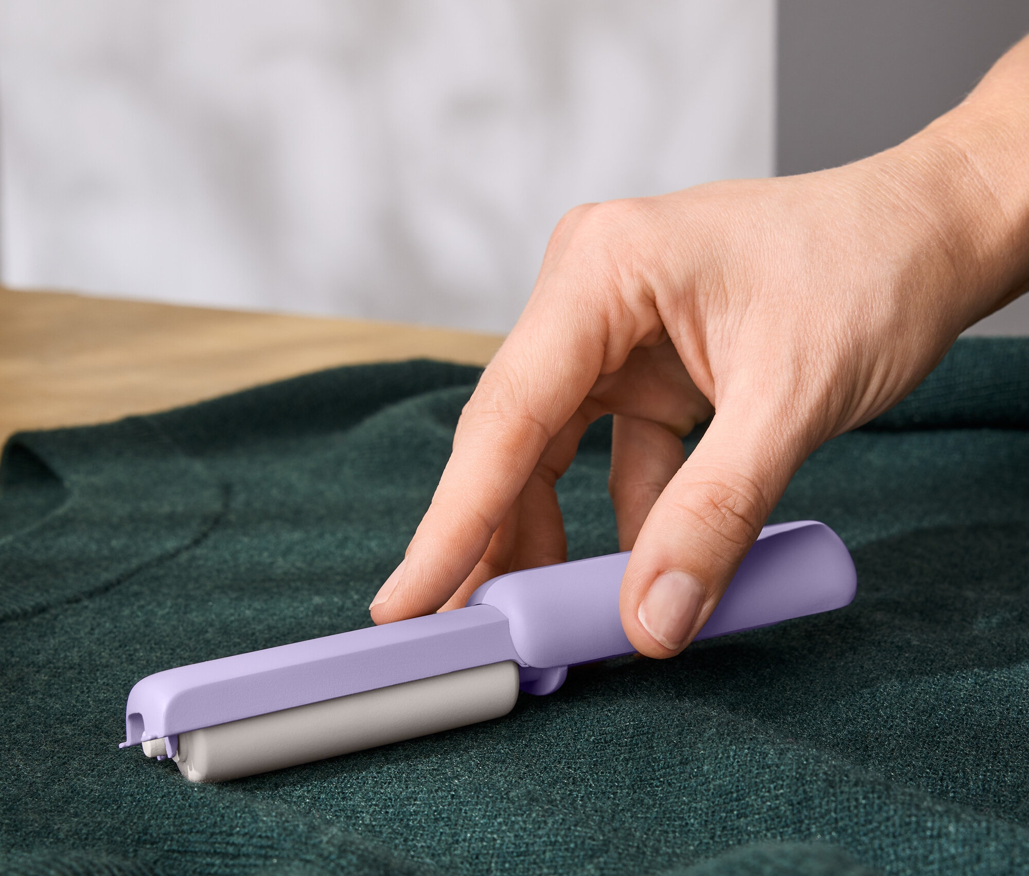 Ruka používá fialový odstraňovač chloupků na zeleném svetru.