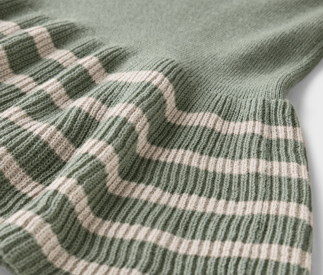 Detail zeleného svetru s krémovými pruhy.