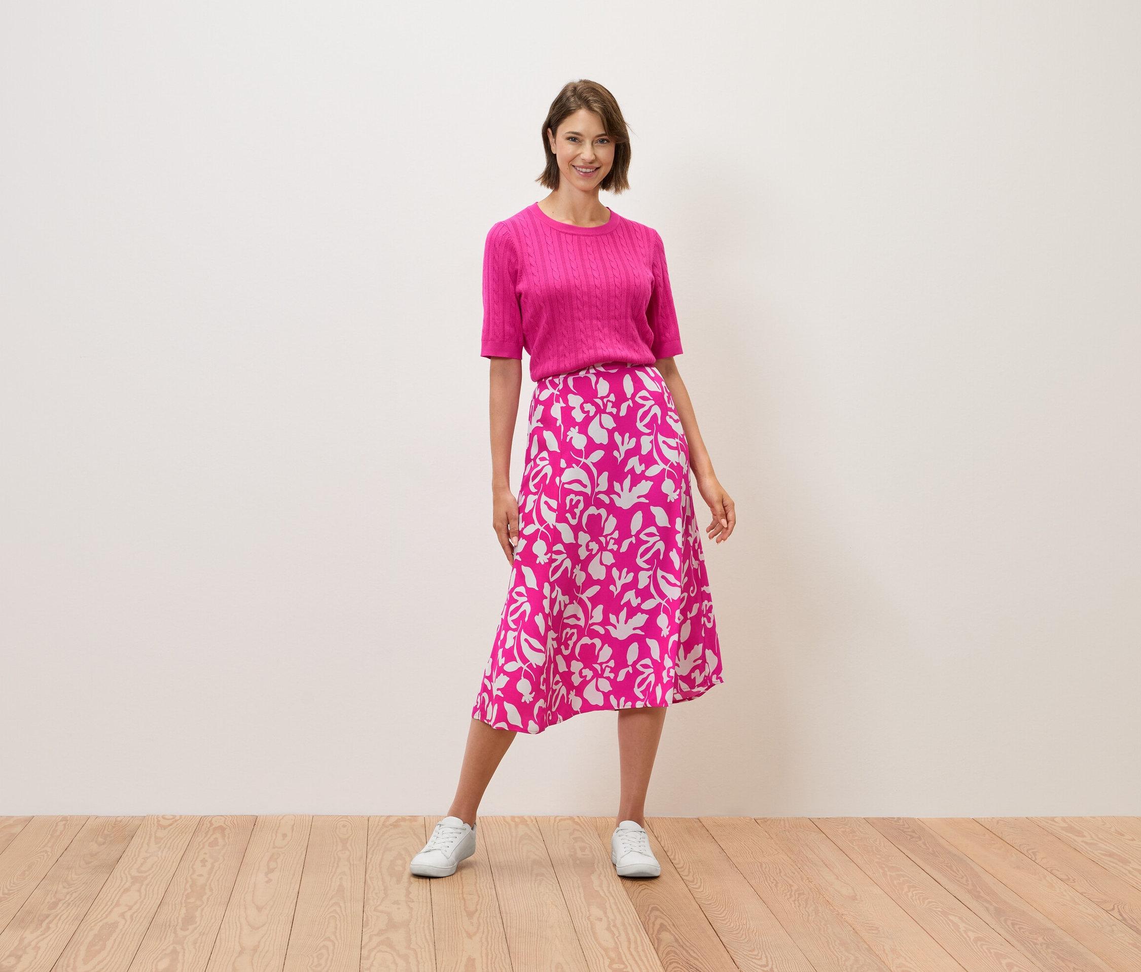 Žena stojí a má na sobě růžový top a sukni s květinovým vzorem.