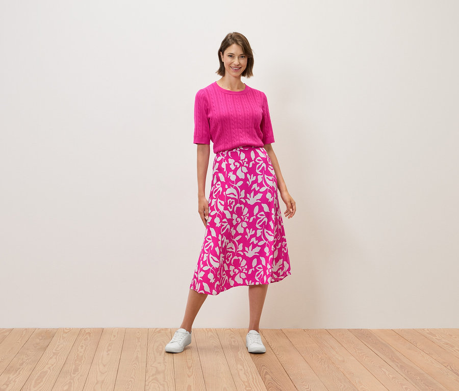 Žena stojí a má na sobě růžový top a sukni s květinovým vzorem.