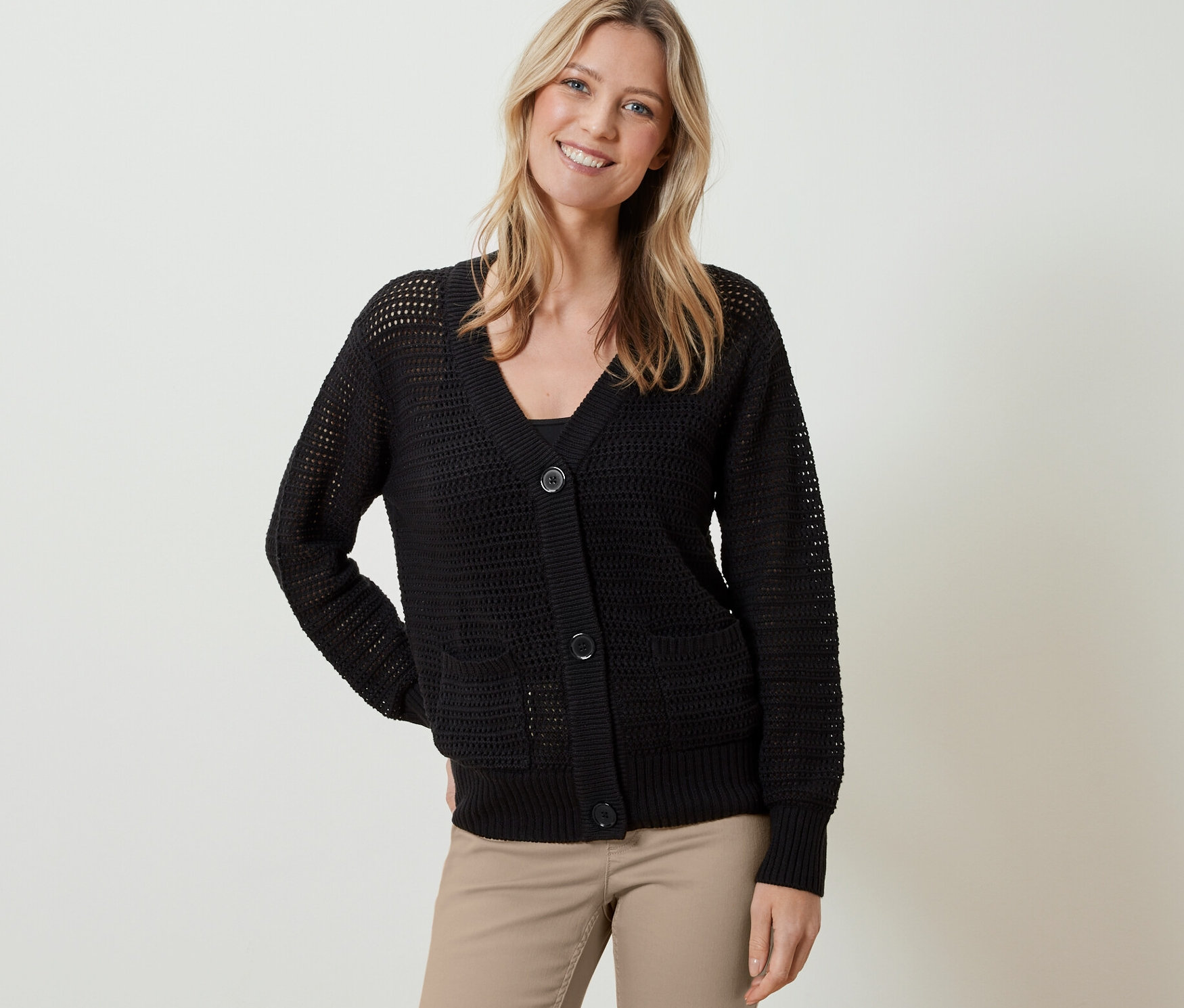 Žena má na sobě černý kardigan z úpletu pointelle a béžové kalhoty.