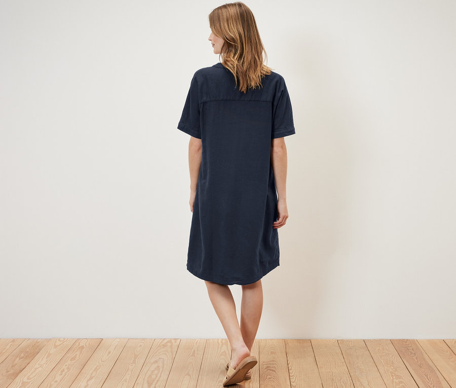 Žena stojí zády k kameře a má na sobě lněné šaty.