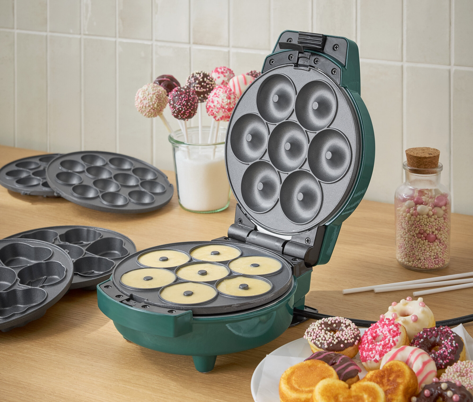 Zelený výrobník na donuty s těstem a talířem hotových donutů.