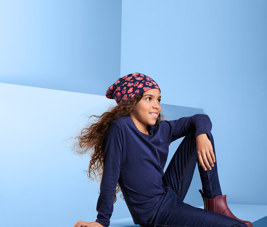 Dívka sedí na modrém pozadí a má na sobě oboustrannou čepici.