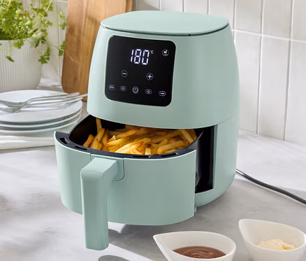 Světle zelená horkovzdušná fritéza o objemu 2 l stojí na kuchyňské lince, naplněná hranolky. Před ní jsou dvě misky s omáčkami.