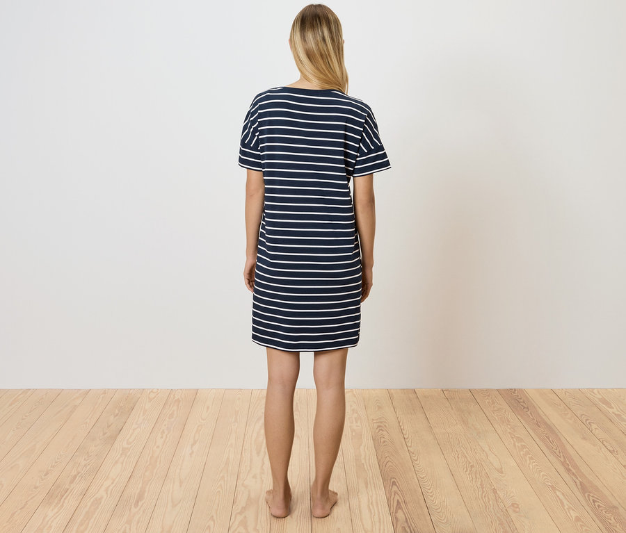 Žena stojí zády k fotoaparátu a má na sobě modré a bílé pruhované tričkové šaty.