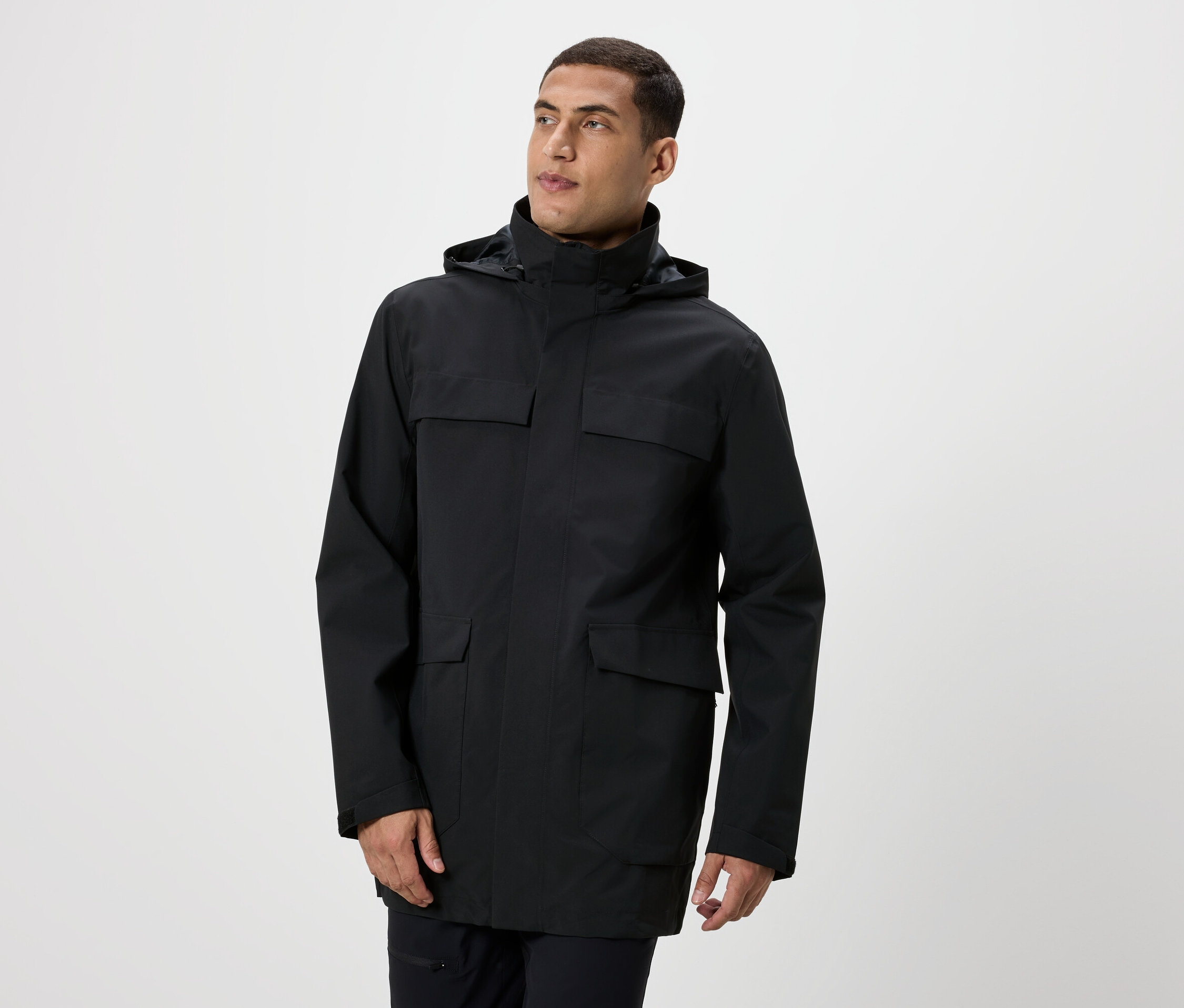 Muž pózuje v černé bundě s kapucí a kapsami.