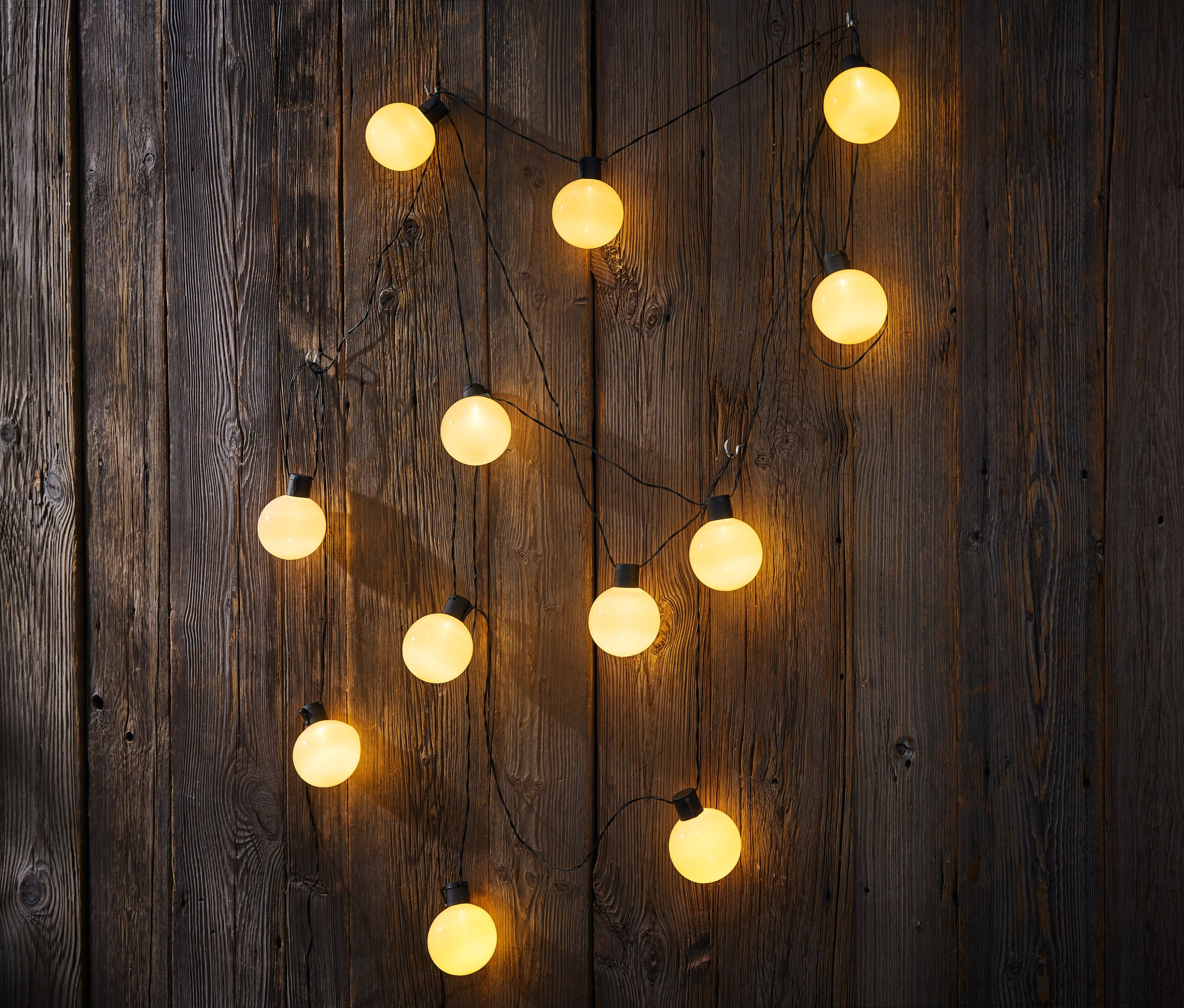 Dva venkovní světelné řetězy s LED diodami visí na dřevěné stěně.