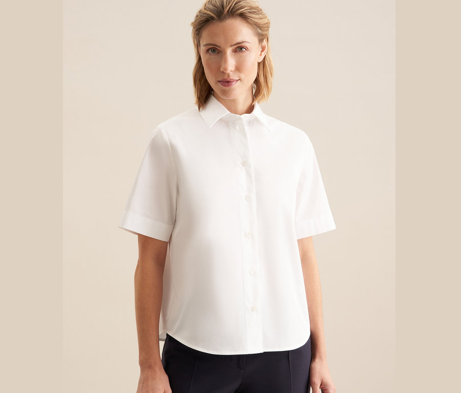 Žena má na sobě bílou halenku s krátkým rukávem Seidensticker.