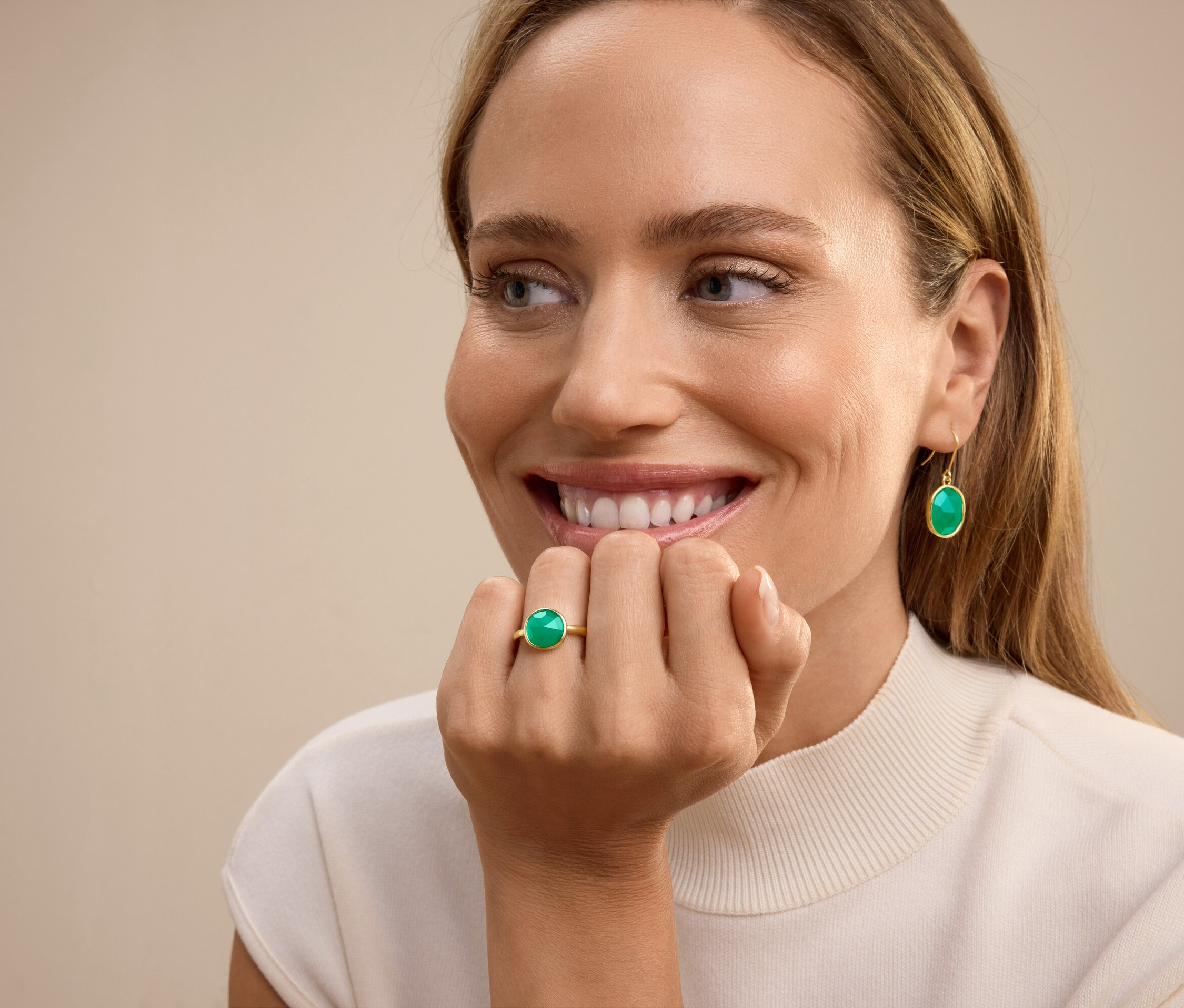 Žena se usmívá, na prsteníčku má prsten se zeleným kamenem a v uších visací náušnice se zeleným kamenem.