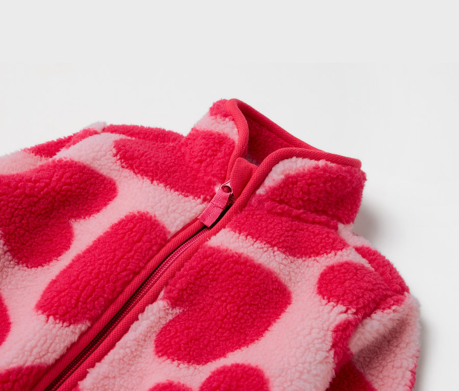 Detail růžové fleecové bundy se zipem a vzorem srdcí.