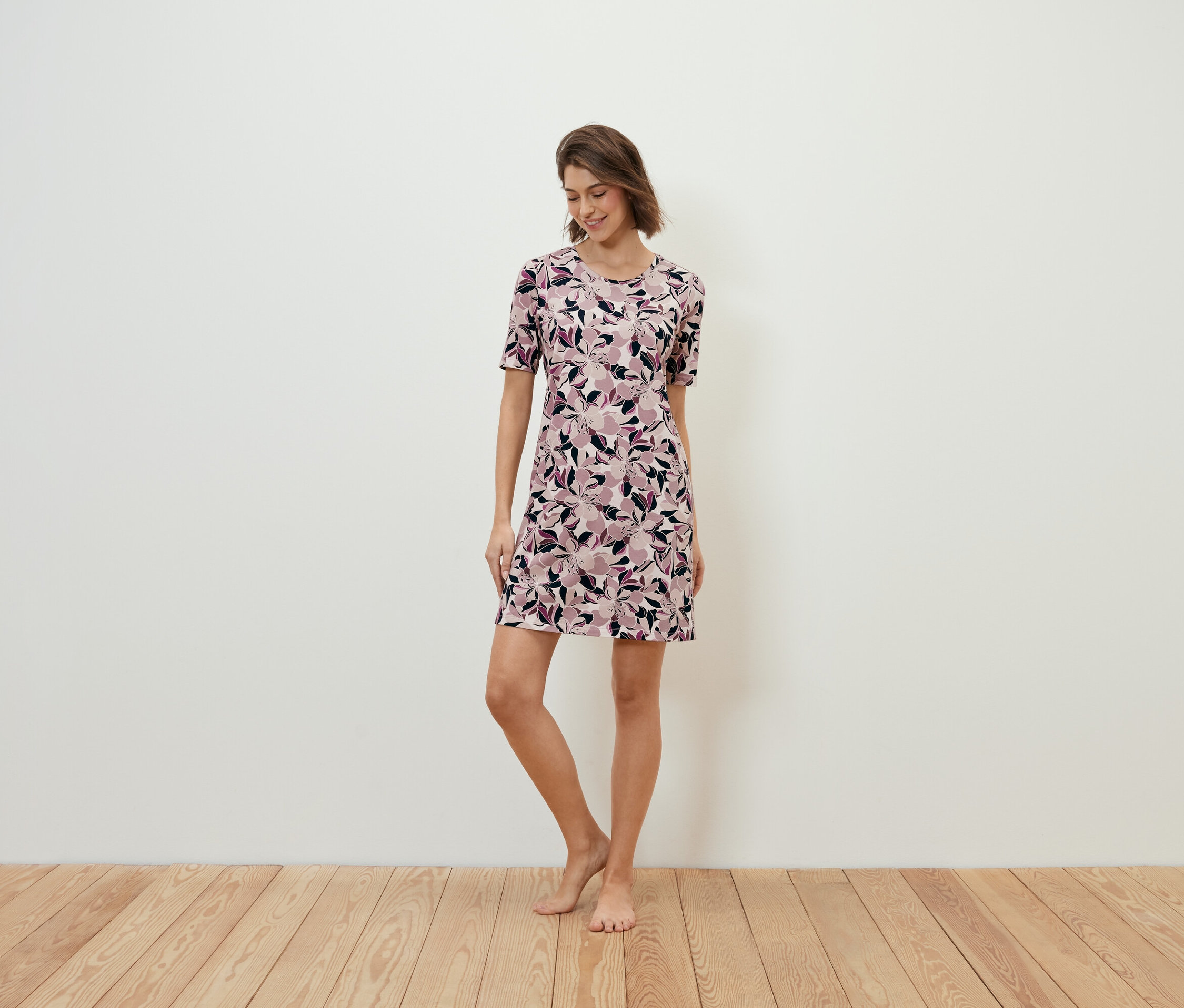 Žena stojí na dřevěné podlaze a má na sobě květinové šaty.