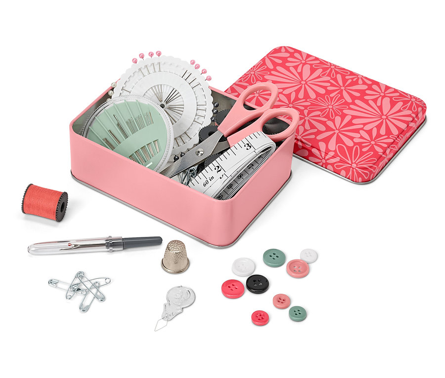 Otevřená kovová krabička s šicí sadou, vedle ní cívka nitě, náprstek, špendlíky, knoflíky a navlékač nitě.