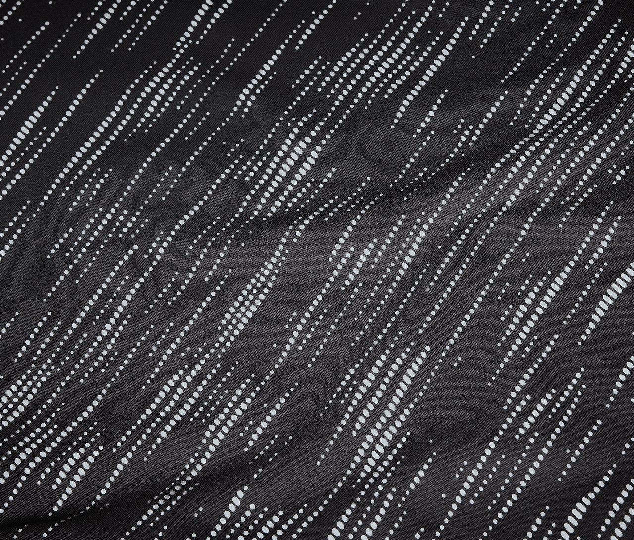 Detailní záběr na černou látku s diagonálními bílými tečkovanými liniemi.