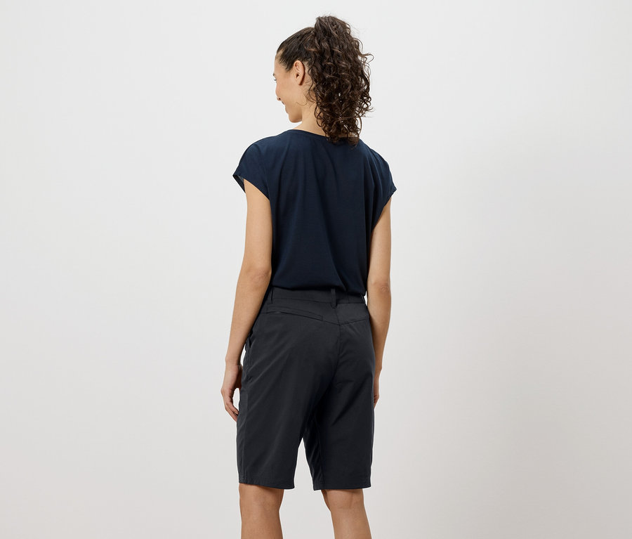 Pohled zezadu na ženu s kudrnatými vlasy, oblečenou v tmavě modrém tričku a šortkách.