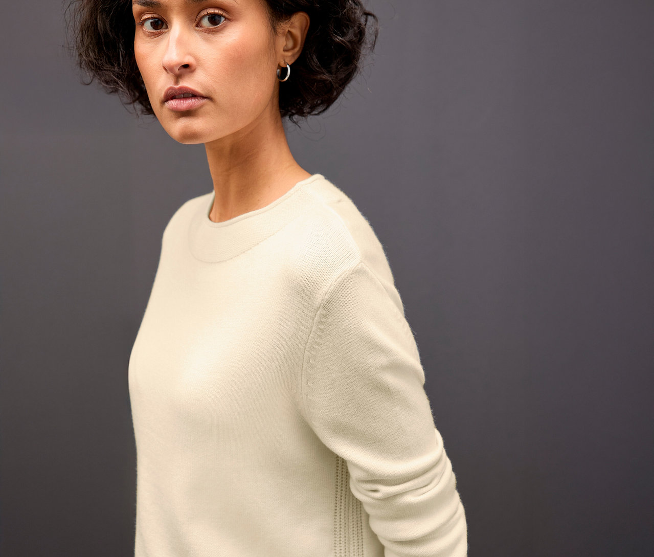 Žena má na sobě béžový pletený svetr s rolovaným lemem Street One.