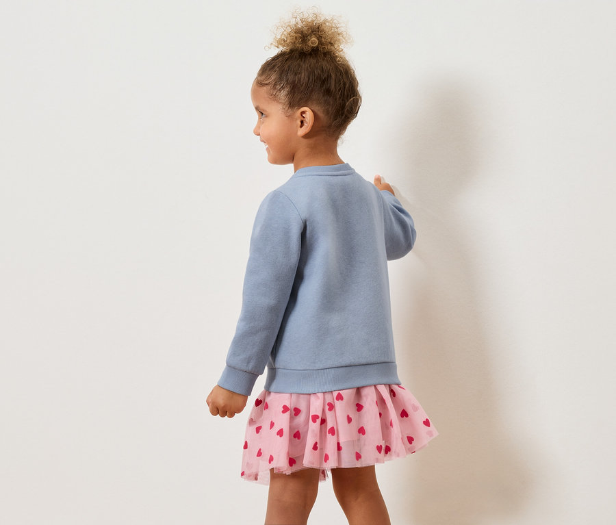 Dívka zezadu v modrém svetru a růžové sukni se srdíčky.