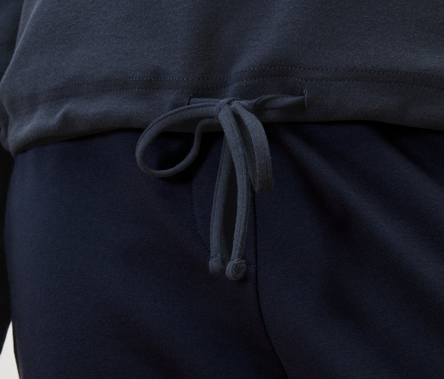 Detailní pohled na tmavě modrý top se stahovací šňůrkou nad tmavě modrými kalhotami.