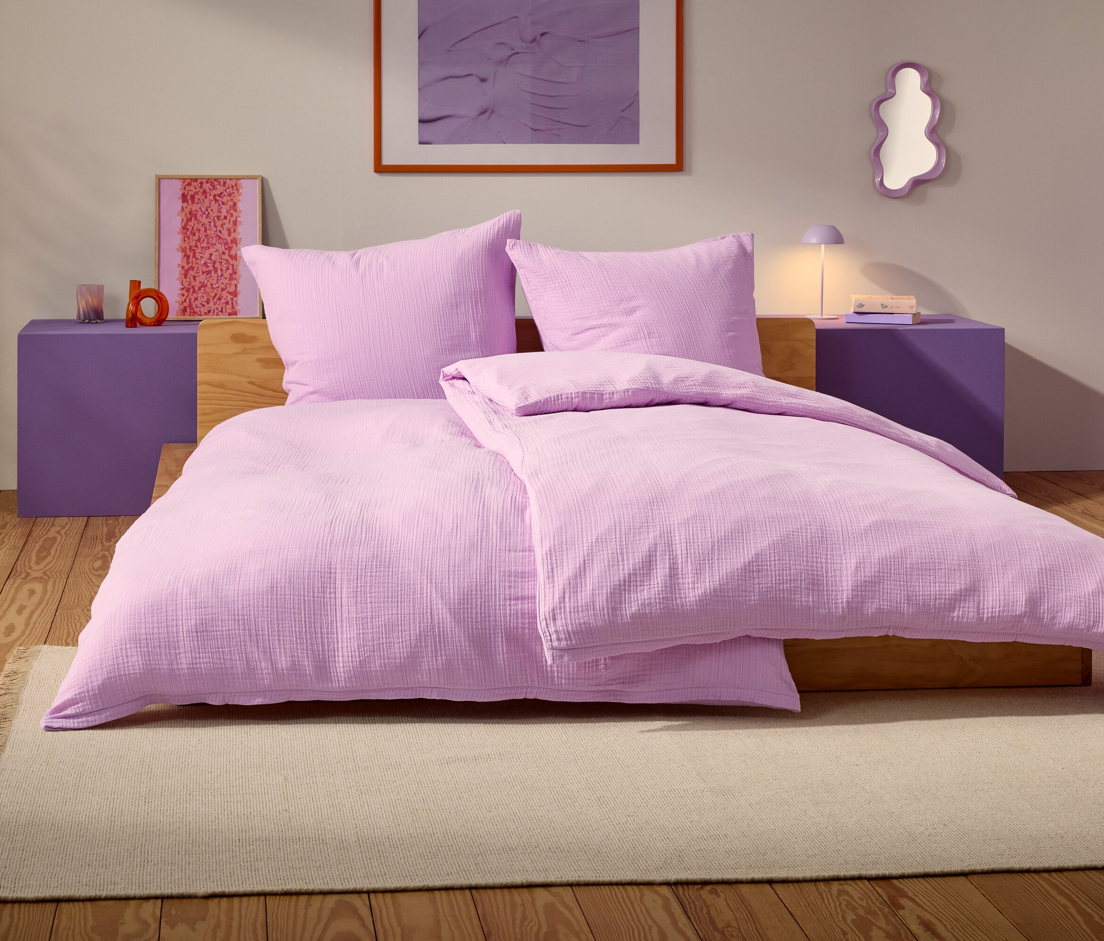 Fialová postel se dvěma polštáři a přikrývkou stojí na béžovém koberci v ložnici.