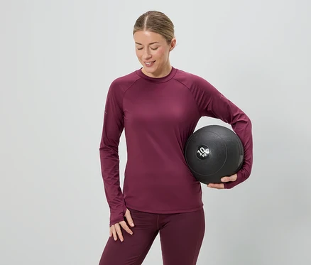 Žena v bordovém sportovním oblečení drží 10 kg medicinbal na šedém pozadí.