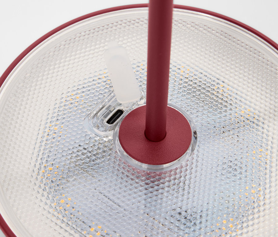 Detailní pohled na lampu s červeným okrajem a stojanem stojící na texturovaném povrchu.