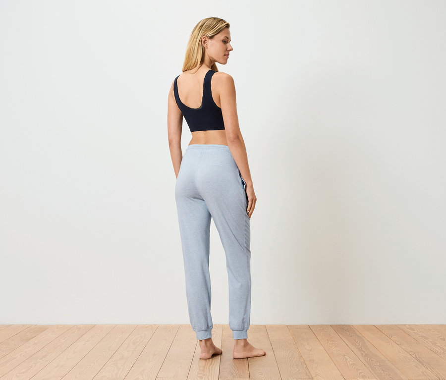 Žena stojí zády, má na sobě černou sportovní podprsenku a světle modré tepláky.