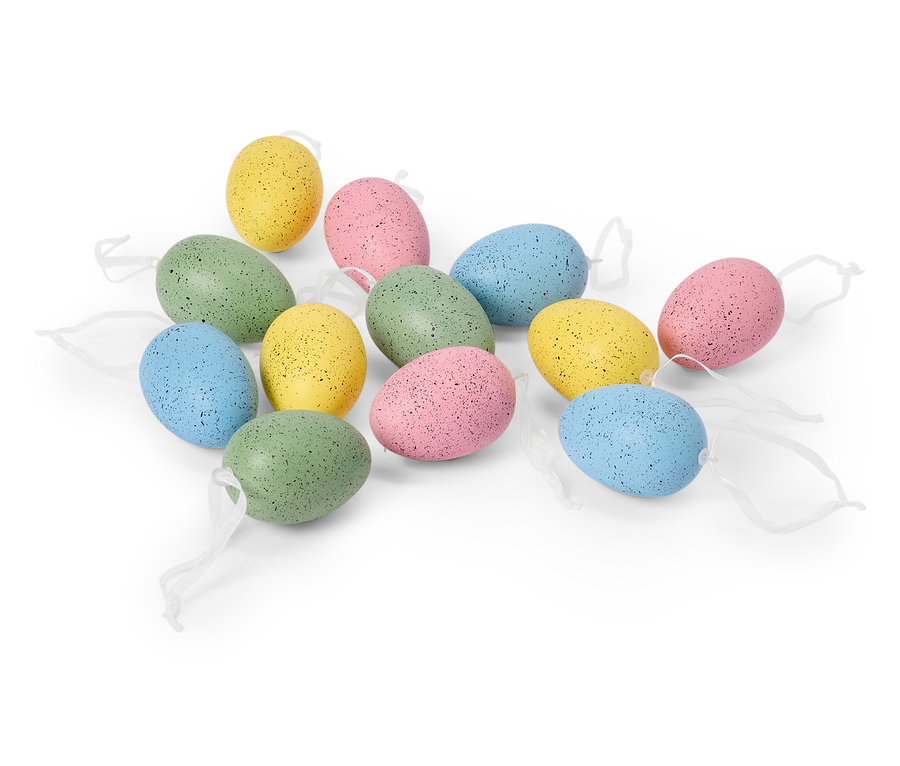 Na bílém pozadí leží tucet pastelových velikonočních vajíček s bílými stuhami.