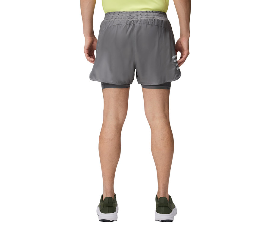 Muž zezadu v šedých šortkách a zelených botách.