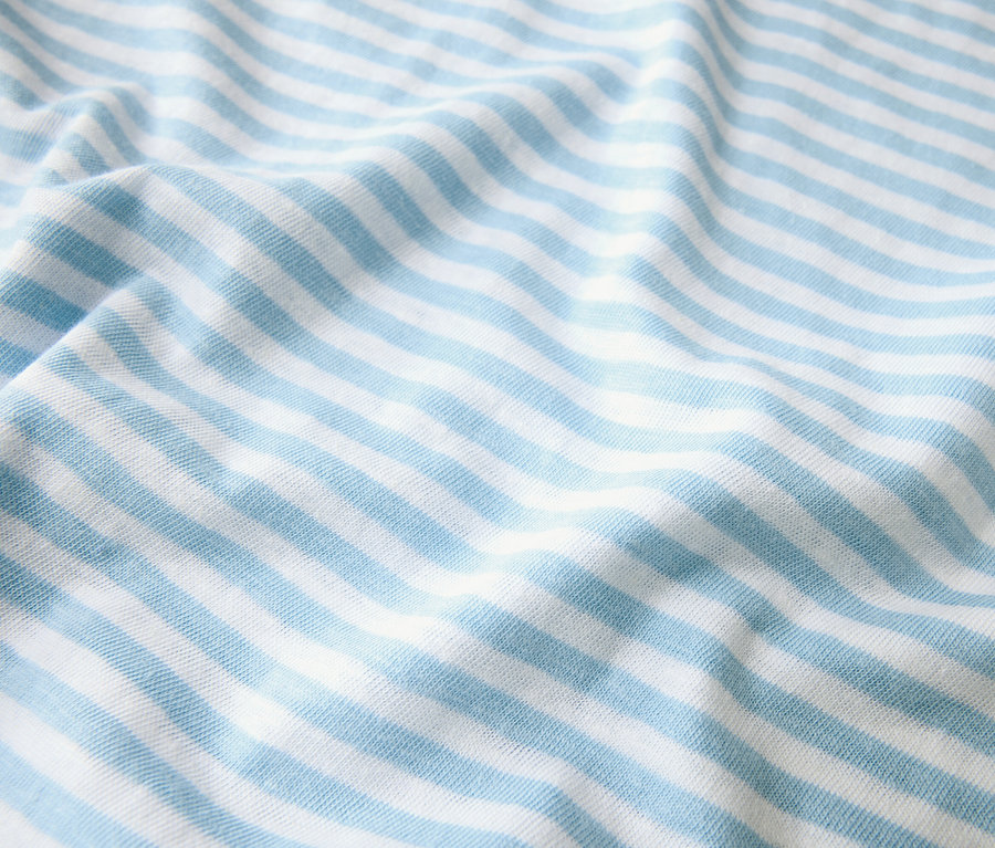 Detailní záběr látky se světle modrými a bílými pruhy, která je poskládaná.