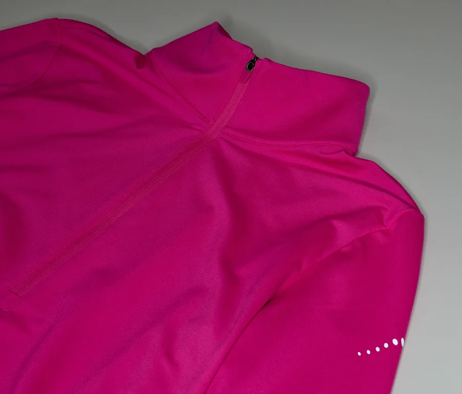 Detail růžového trička s dlouhým rukávem, límcem na zip a reflexními tečkami na rukávu.