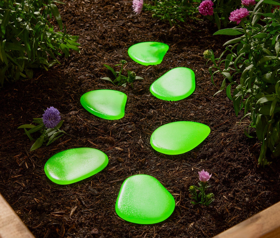 Zelené okrasné kameny leží v záhonu mezi rostlinami.