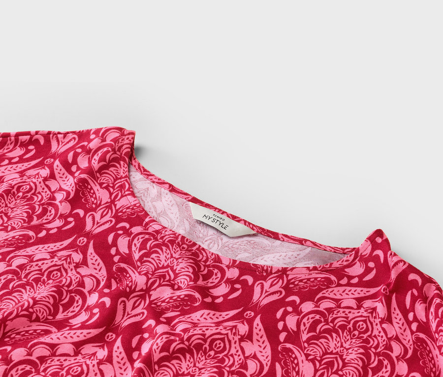 Detailní záběr výstřihu červeno-růžového vzorovaného topu se štítkem 'TCHIBO MY STYLE'.