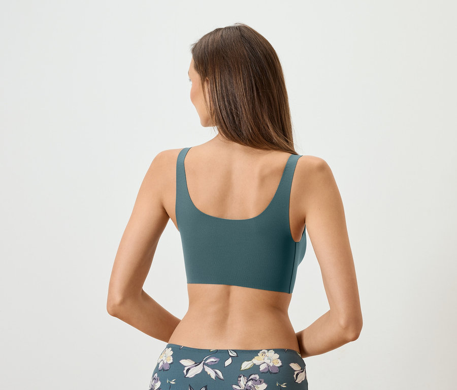 Pohled zezadu na ženu s dlouhými hnědými vlasy, která má na sobě petrolejovou sportovní podprsenku a květinové legíny.