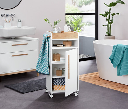 V koupelně stojí bílá skříňka pod umyvadlo Eklund se dvěma zásuvkami, úložný stojánek, dávkovač tekutého mýdla, froté osuška, žakárové ručníky (2 ks), froté ručníky (2 ks, antracitové), dózy z bambusu (2 ks), dekorační kameny s LED (2 ks) a koupelnový odkládací vozík Eklund.