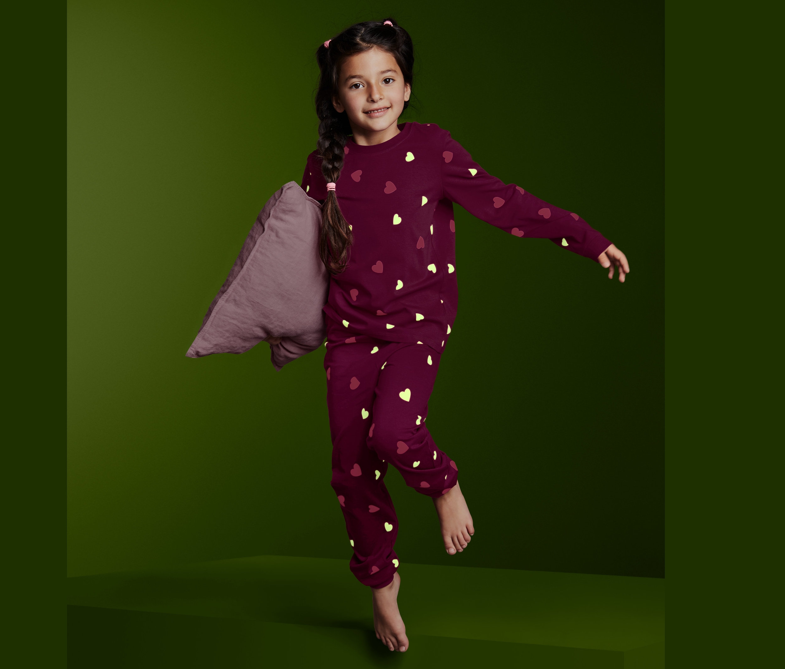 Dívka skáče a drží polštář, má na sobě pyžamo Glow in the dark.