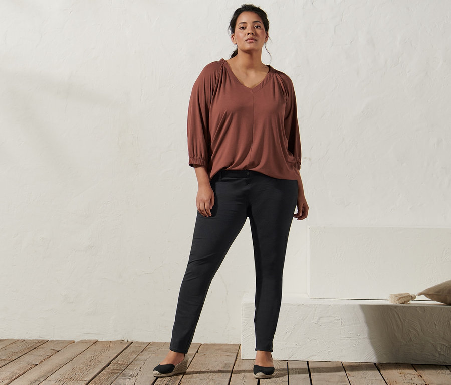 Žena pózuje v terakotové halence s řasením, džeginách a espadrilkách s klínovým podpatkem.