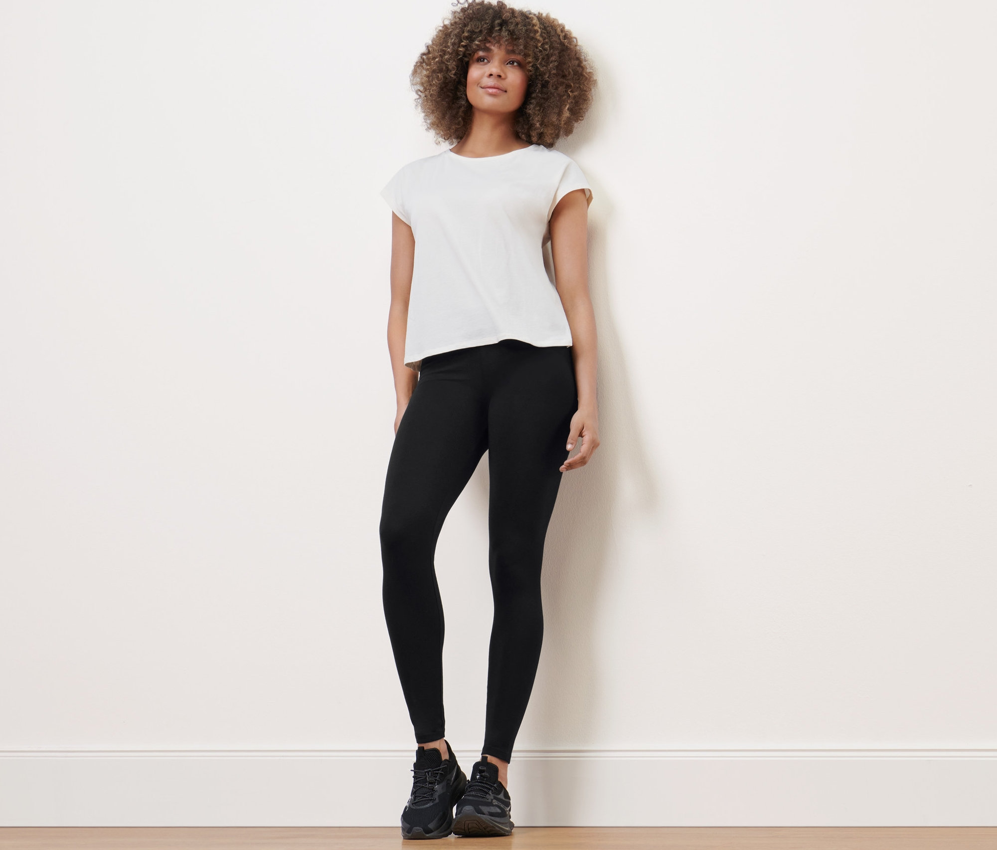 Žena stojí a má na sobě sportovní legíny, tričko a tenisky.