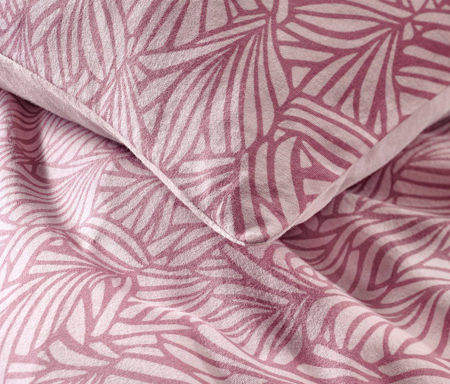 Detailní záběr na polštář a přikrývku s geometrickým květinovým vzorem. Jedná se o povlečení ze zimního žerzeje.