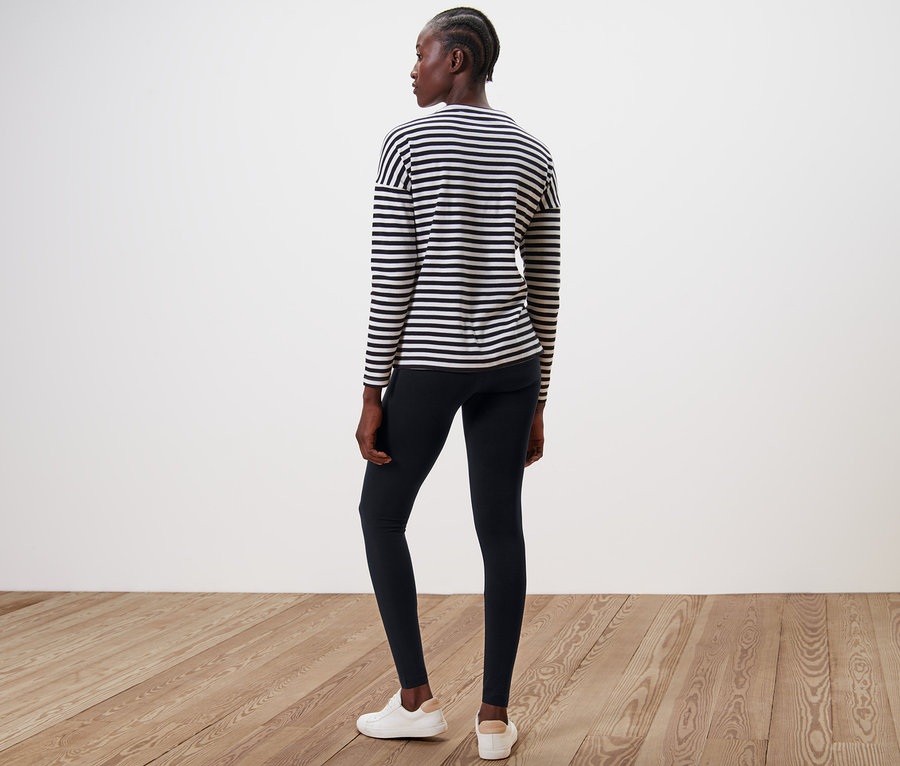 Žena stojí zády k fotoaparátu a má na sobě černé legíny a pruhované tričko.