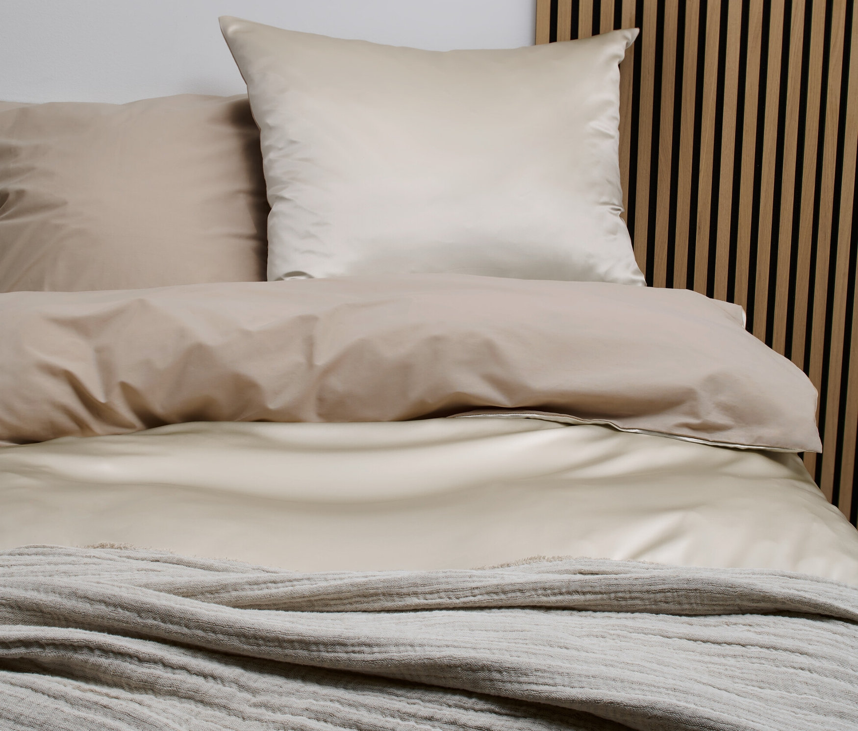 Ložní souprava z hedvábí a bavlny standardní velikosti na posteli s dřevěným čelem.