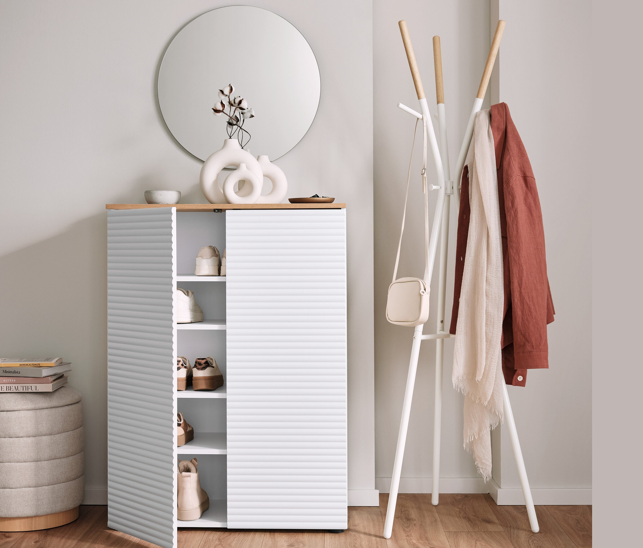 Botník s otevřenými dveřmi vedle věšáku na šaty a pufu s úložným prostorem.