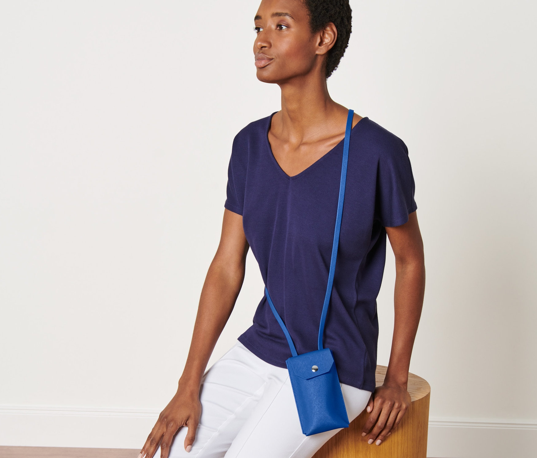 Žena sedí na dřevěné stoličce a má na sobě modrou mini kabelku.