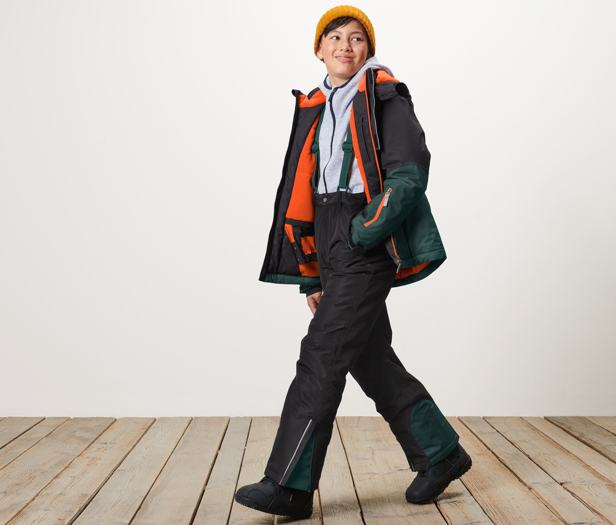 Chlapec v žluté čepici kráčí a má na sobě černé lyžařské kalhoty.