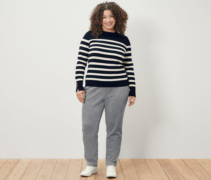 Žena má na sobě tmavě modrý proužkovaný svetr z jemného úpletu a kalhoty joggpant.