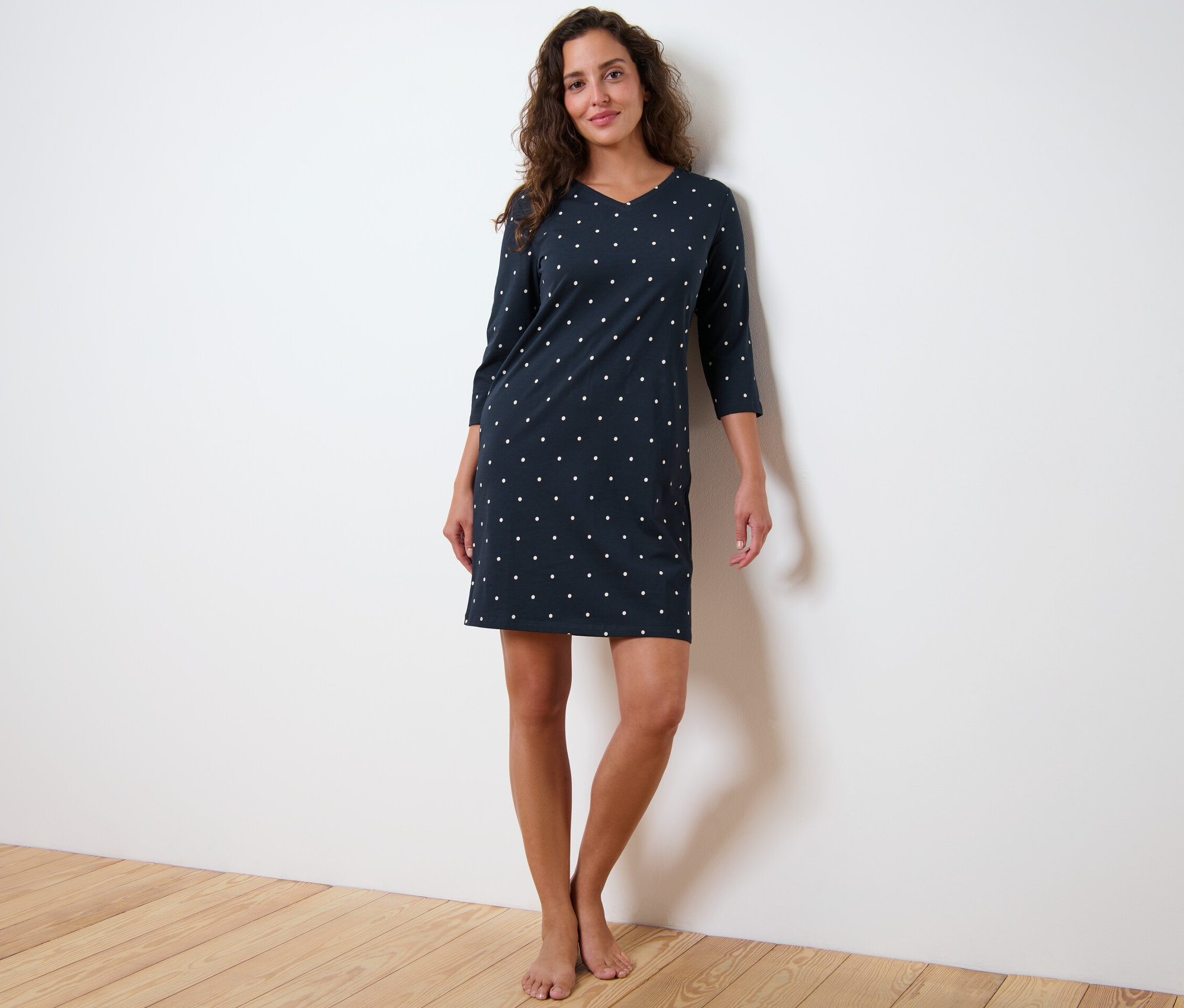 Žena stojí a má na sobě noční košili s tříčtvrtečním rukávem a puntíky.
