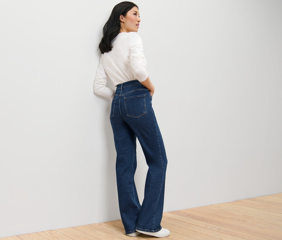 Žena pózuje v tmavě modrých džínách bootcut střihu »Lou« a bílém topu s dlouhým rukávem.