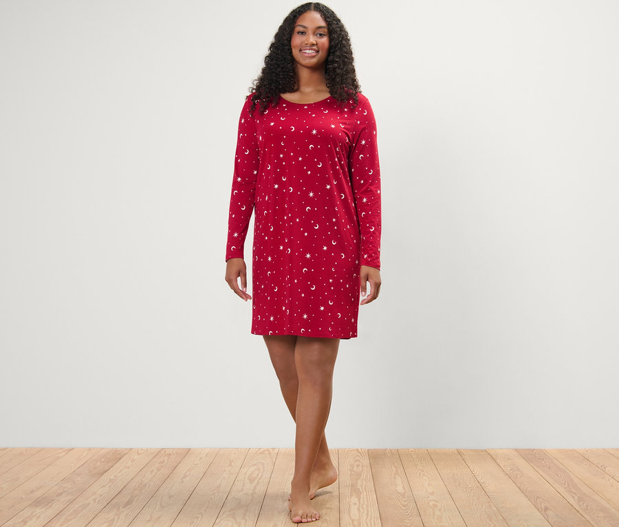 Žena stojí a usmívá se na kameru v červené noční košili.